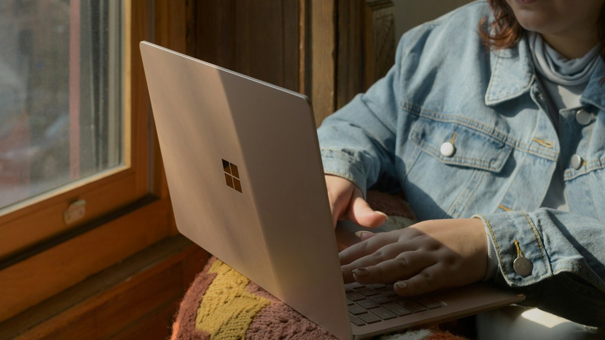 A woman sitting with a Windows laptop and typing on it.